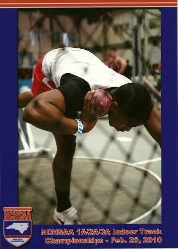High school athlete preparing for shot put throw at indoor track championships, wearing a white and.
