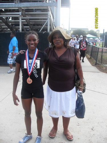 Young female athlete with medal and woman at track event, smiling outdoors.