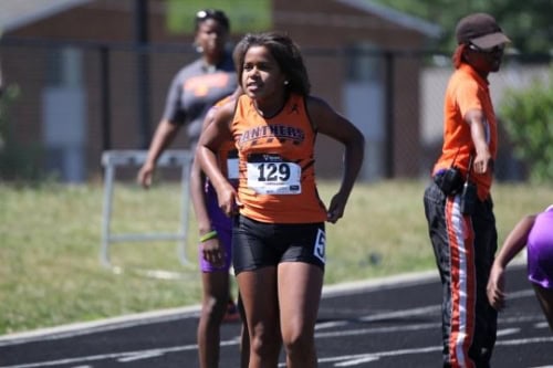 Running athlete wearing Panthers Elite uniform on a track during a race.
