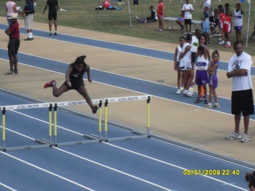 Young female athlete jumping over hurdles at a track meet.