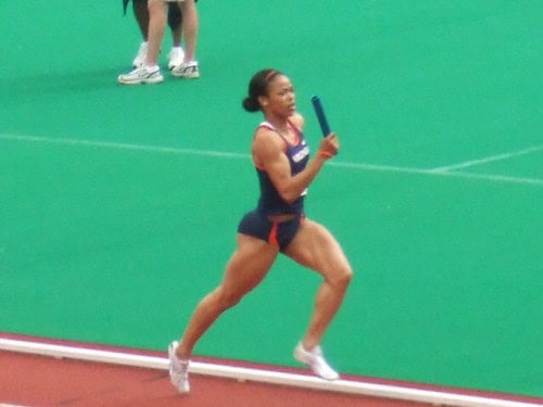 Female athlete running with baton on indoor track at Panthers Elite Track & Field Club.