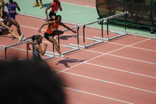 Young female athletes competing in hurdles at a track meet.