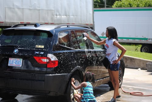 Washing a black BMW X5 SUV with soap and water outdoors.
