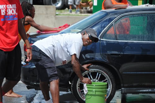 Washing a black sedan with a green bucket during a community event.