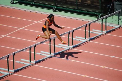 Female hurdler in mid-air during a track and field race at Charlotte stadium.