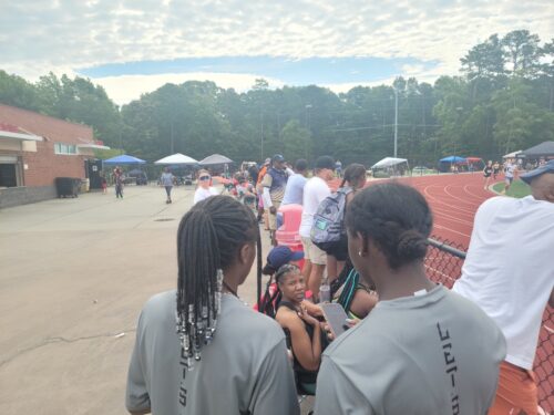Group of young athletes and coaches at a track and field event outdoors.