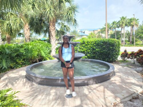 Young female athlete standing by a fountain outdoors, smiling.