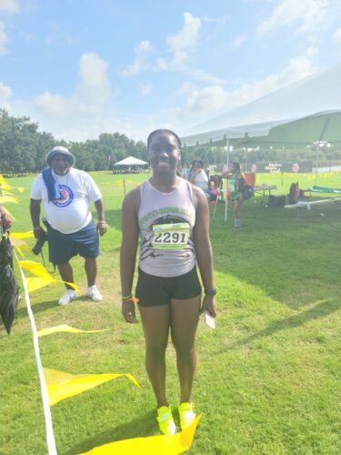 Athlete smiling at a track and field event, wearing a white tank top and black shorts.