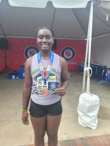 Athlete with medals at a track event, smiling and holding awards.