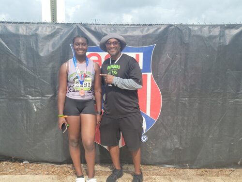 Two athletes celebrating after a track event with medals and coach.