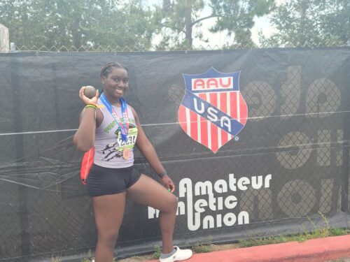 Young female athlete holding a medal and a ball at a track event.