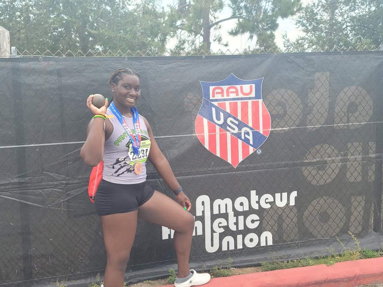 Young female athlete holding a medal and a ball at a track event.