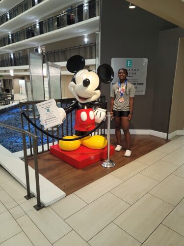Mickey Mouse statue with girl at indoor mall, near pool area, promoting family fun and entertainment.