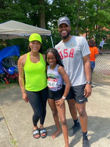 Young athlete with coaches at track event, smiling outdoors.