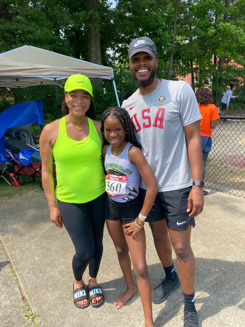 Young athlete with coaches at track event, smiling outdoors.
