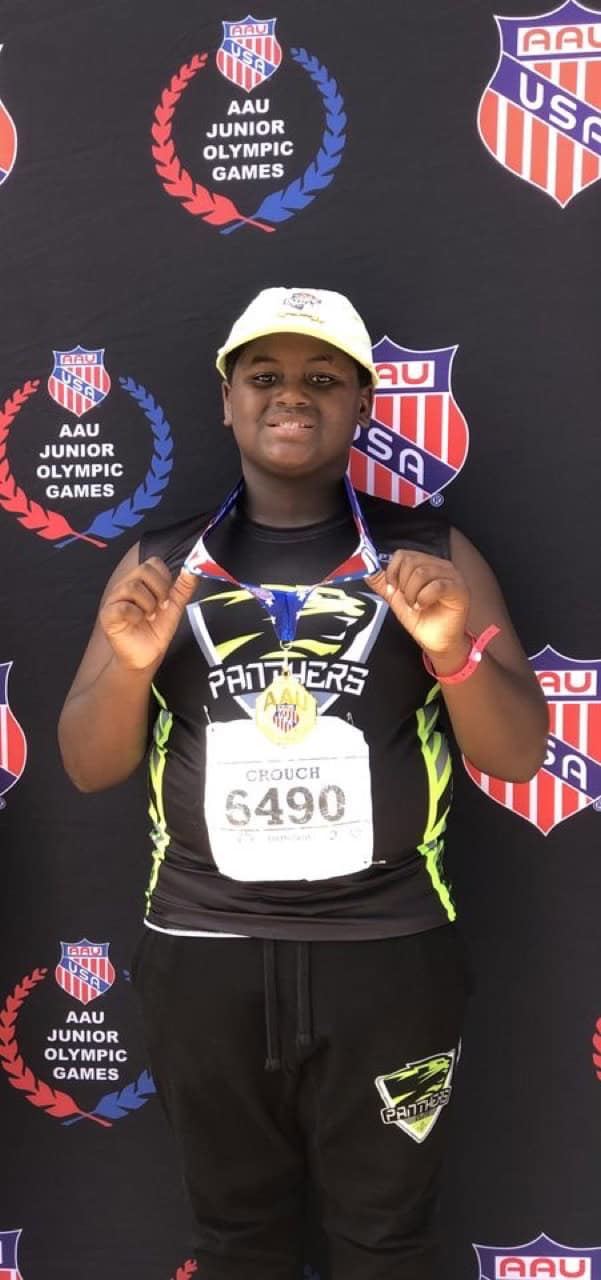 Young athlete holding a medal at the Junior Olympics with Panthers Elite gear.