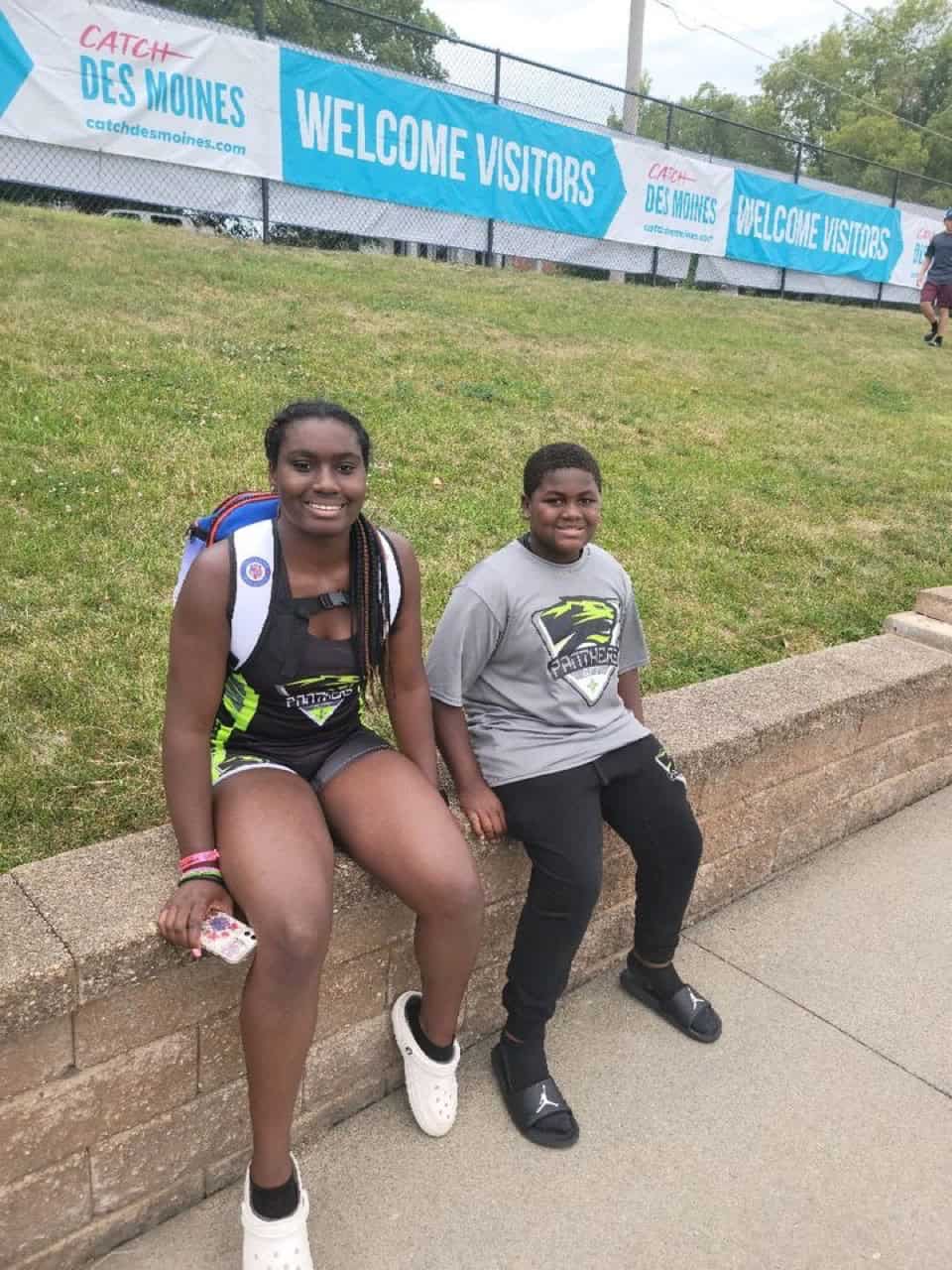 Two young athletes sitting on a brick ledge at a track event.