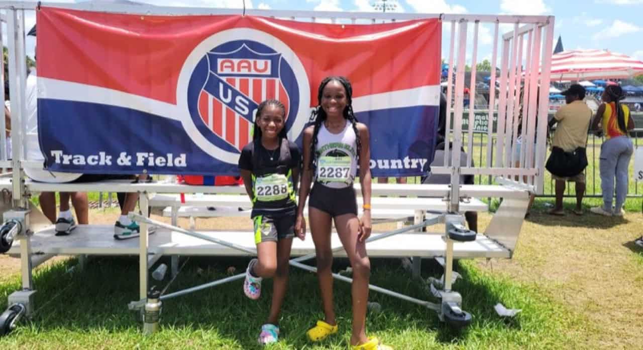 Two young athletes at a track event with a Panthers Elite banner.