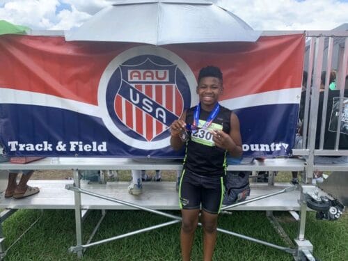 Young athlete smiling with medal at track event.
