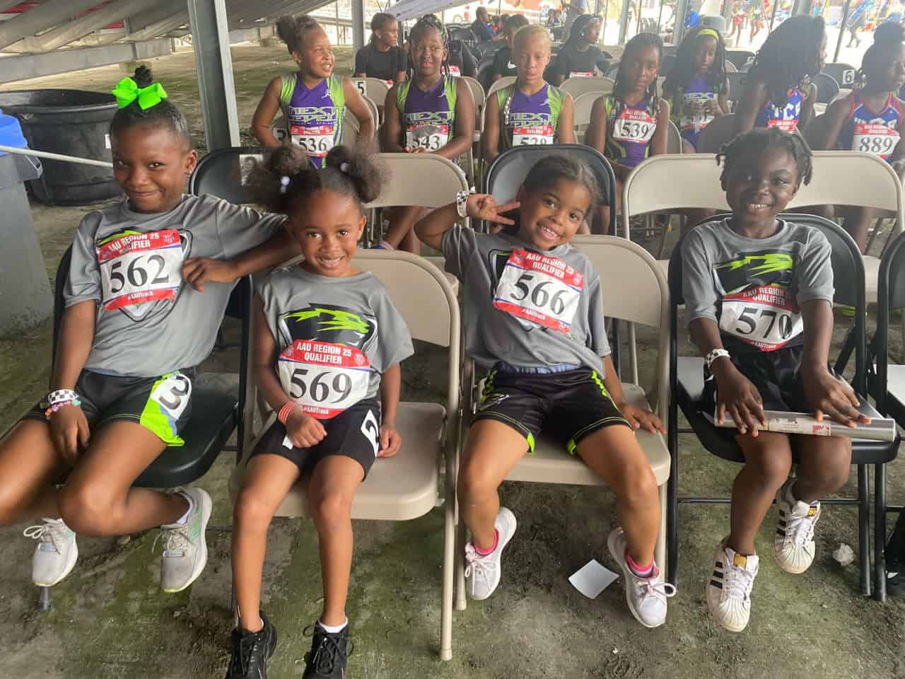 Young track athletes sitting on chairs, smiling, wearing team uniforms.