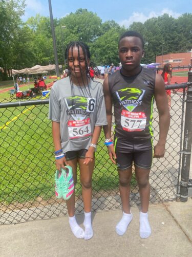Young athletes at a track meet standing by a fence.