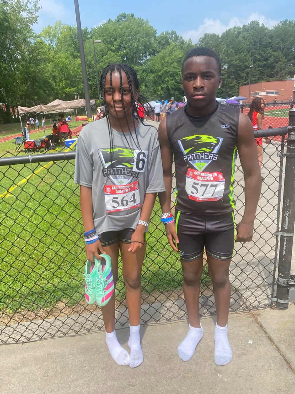 Young athletes at a track meet standing by a fence.