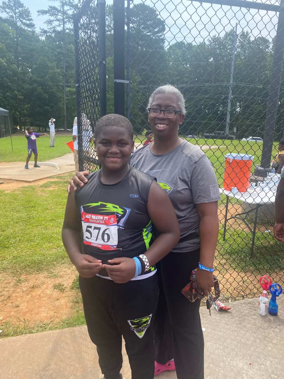 Young athlete with coach at track meet behind fence.