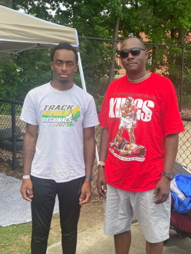 Two young men standing outdoors at a track event, one in a Panthers Elite T-shirt, the other in sung.