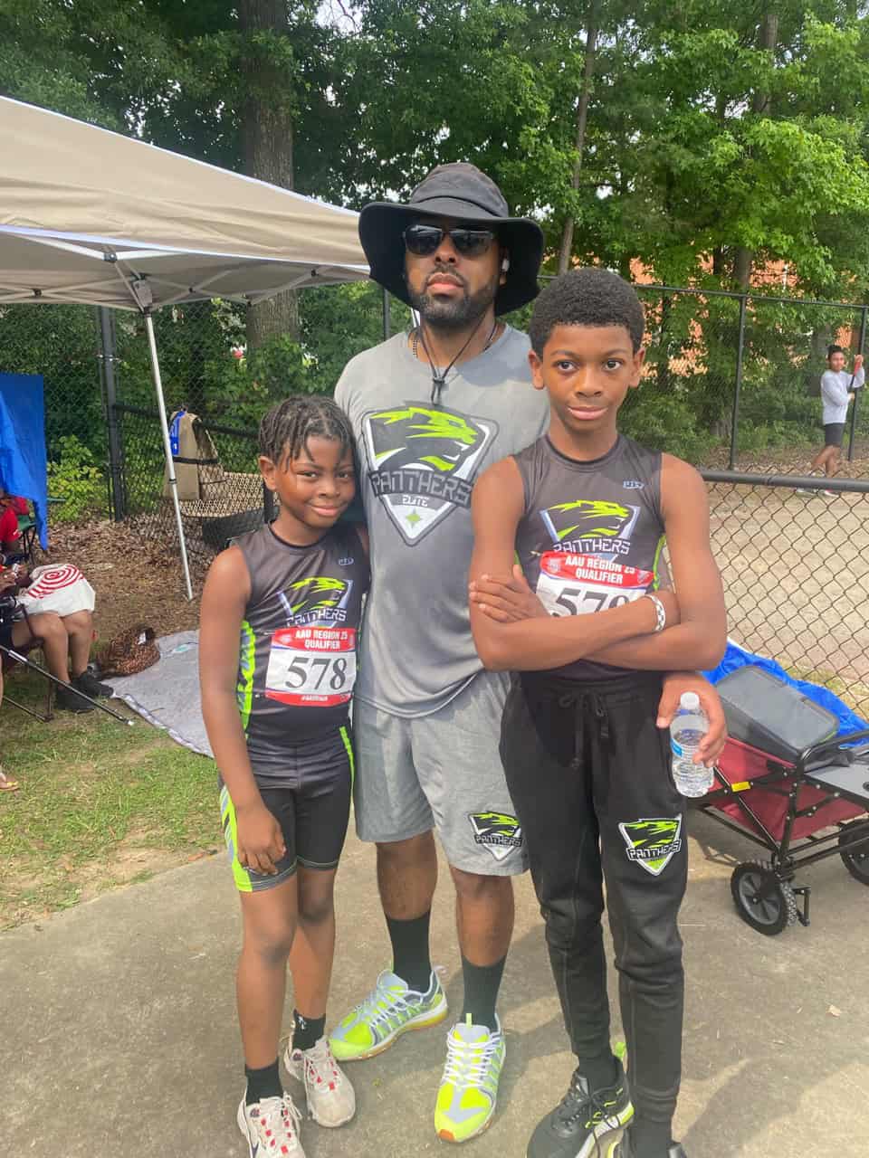 Coach with two young athletes at a track event outdoors.