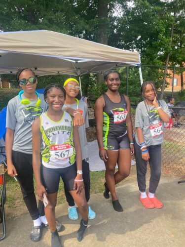 Group of young female athletes at a track event, smiling and ready to race.