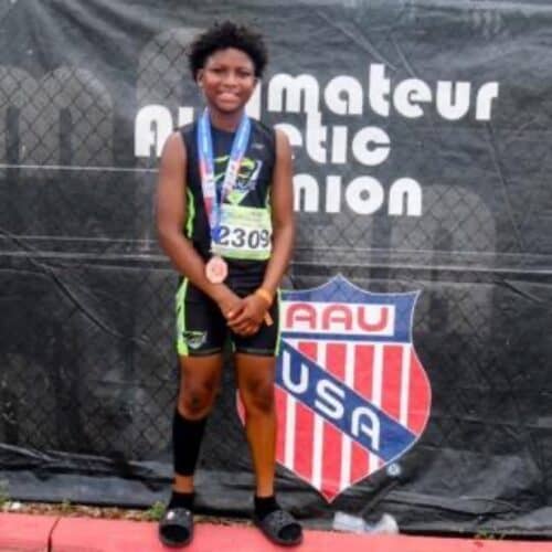 Young athlete with medals at a track event, standing in front of a Panthers Elite banner.