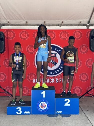 Young athletes celebrating on the winners' podium at a track event.