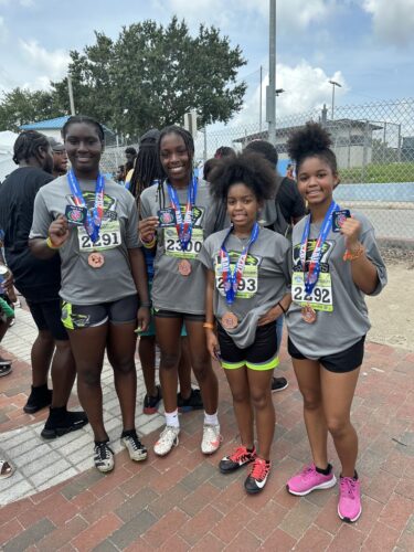 Young female track athletes celebrating with medals after a race.