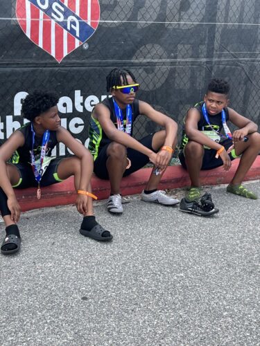 Young track athletes sitting on the ground with medals, after a competition.