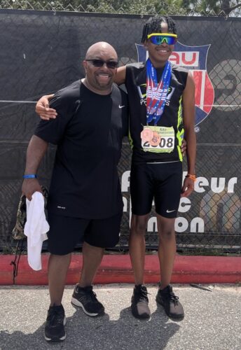 Track athlete with coach after race, wearing medals and sunglasses.