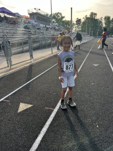 Young girl standing on the track with race bib number 873, smiling confidently.