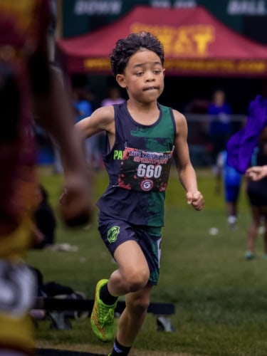 Young boy running in a track and field event, wearing a green and black uniform with the number 660.