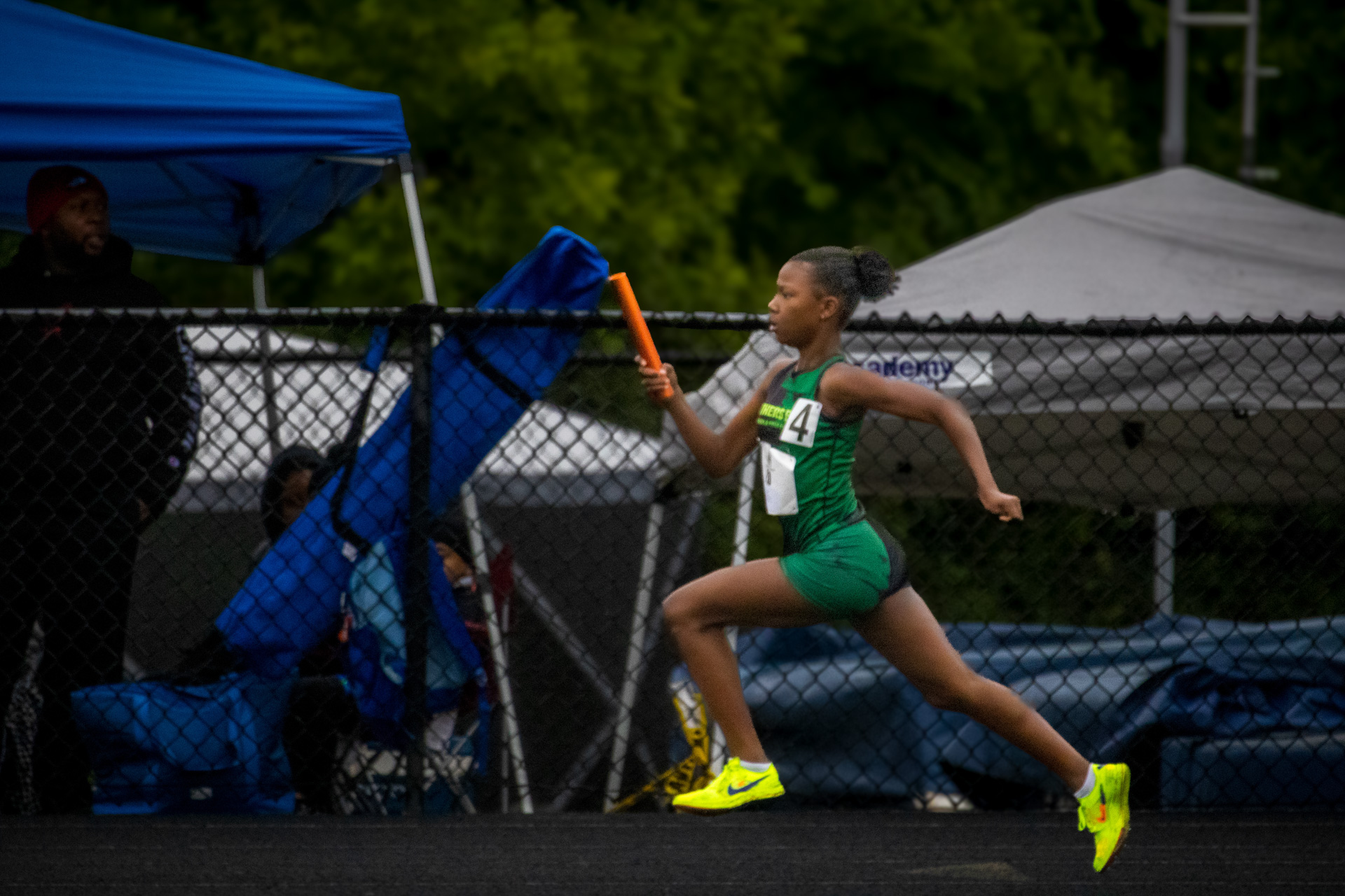 Young female athlete sprinting with baton at track meet.