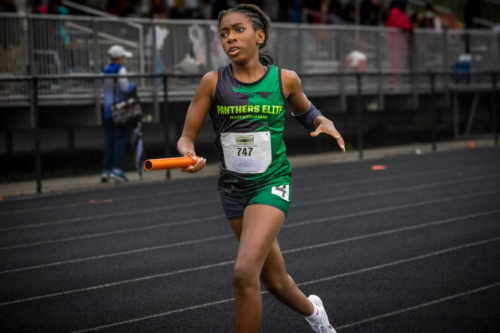 Young female athlete running on track with baton during a race.