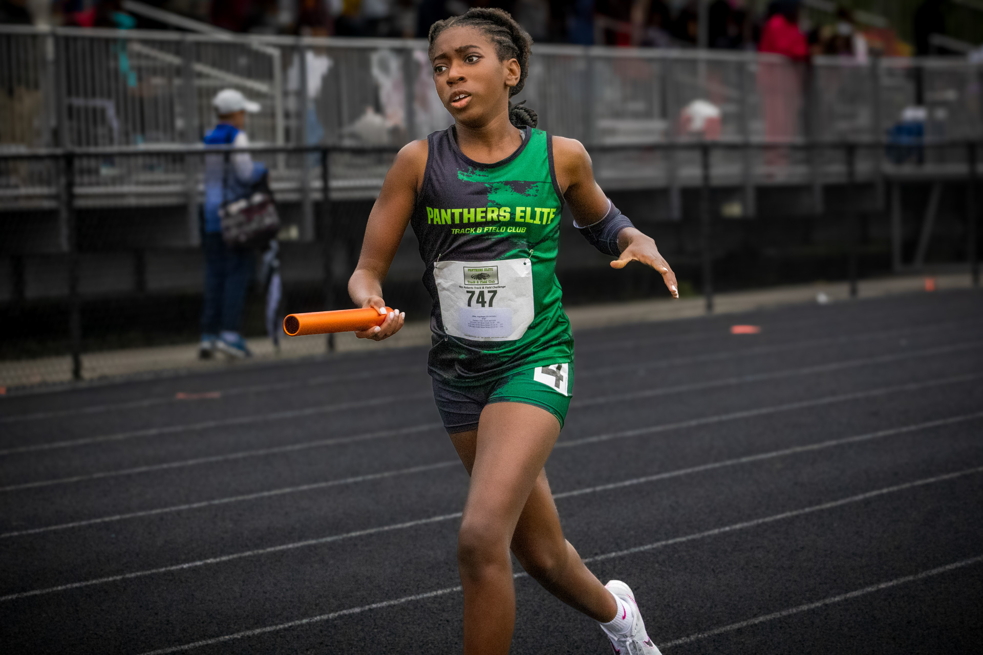 Young female athlete running on track with baton during a race.