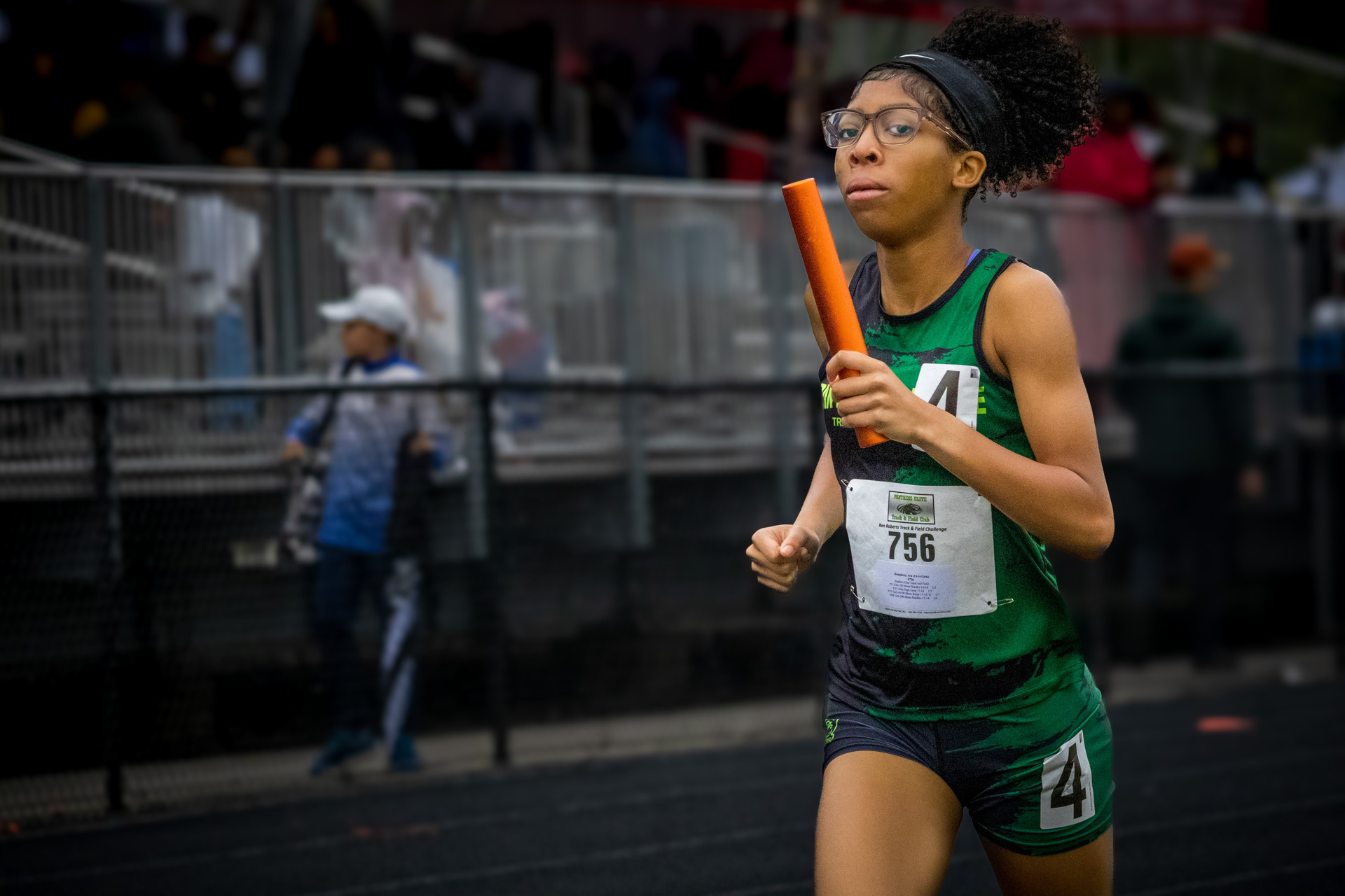 Young female athlete running with baton during track race at Panthers Elite meet.