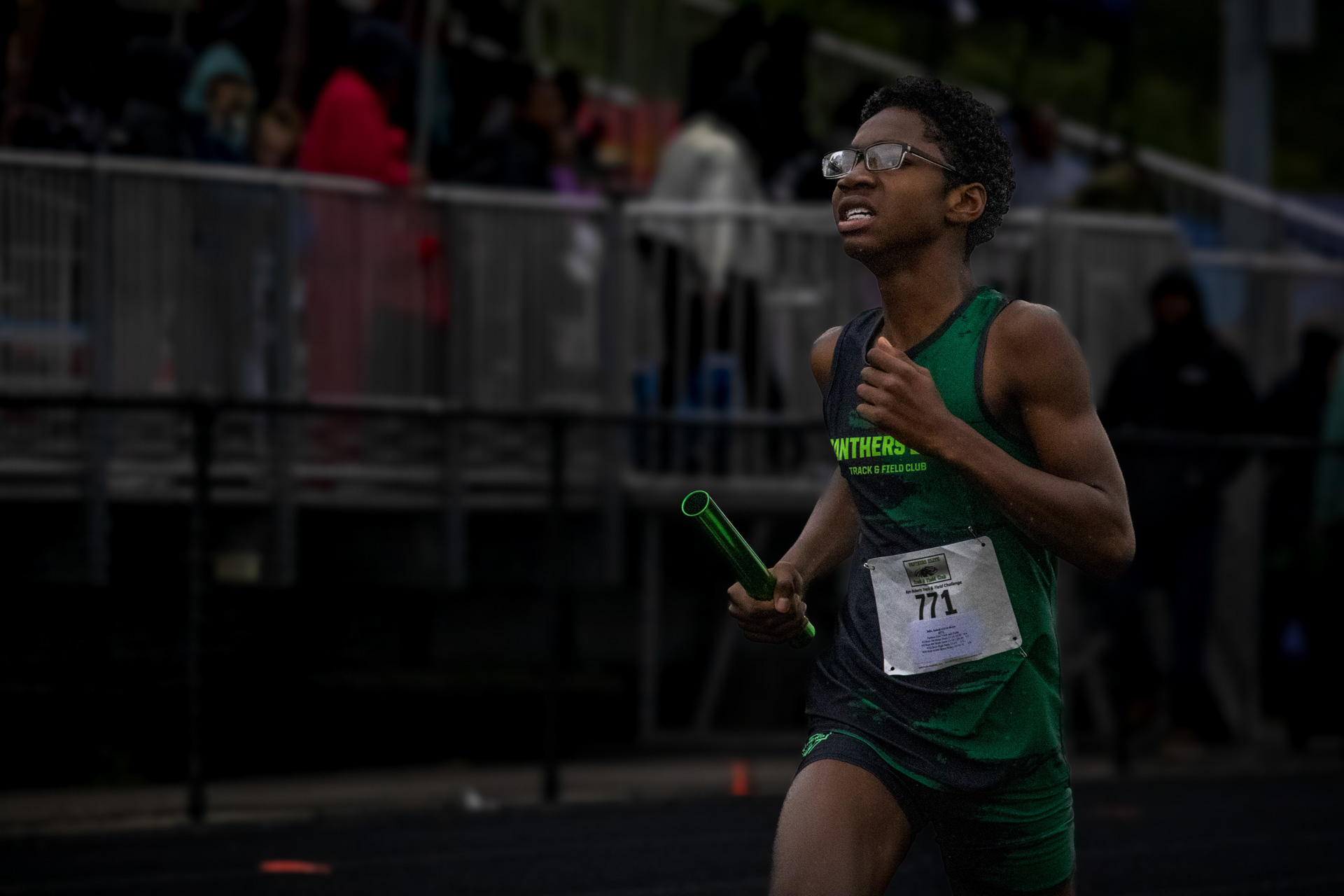 Young athlete running in a track race, wearing green uniform and glasses.