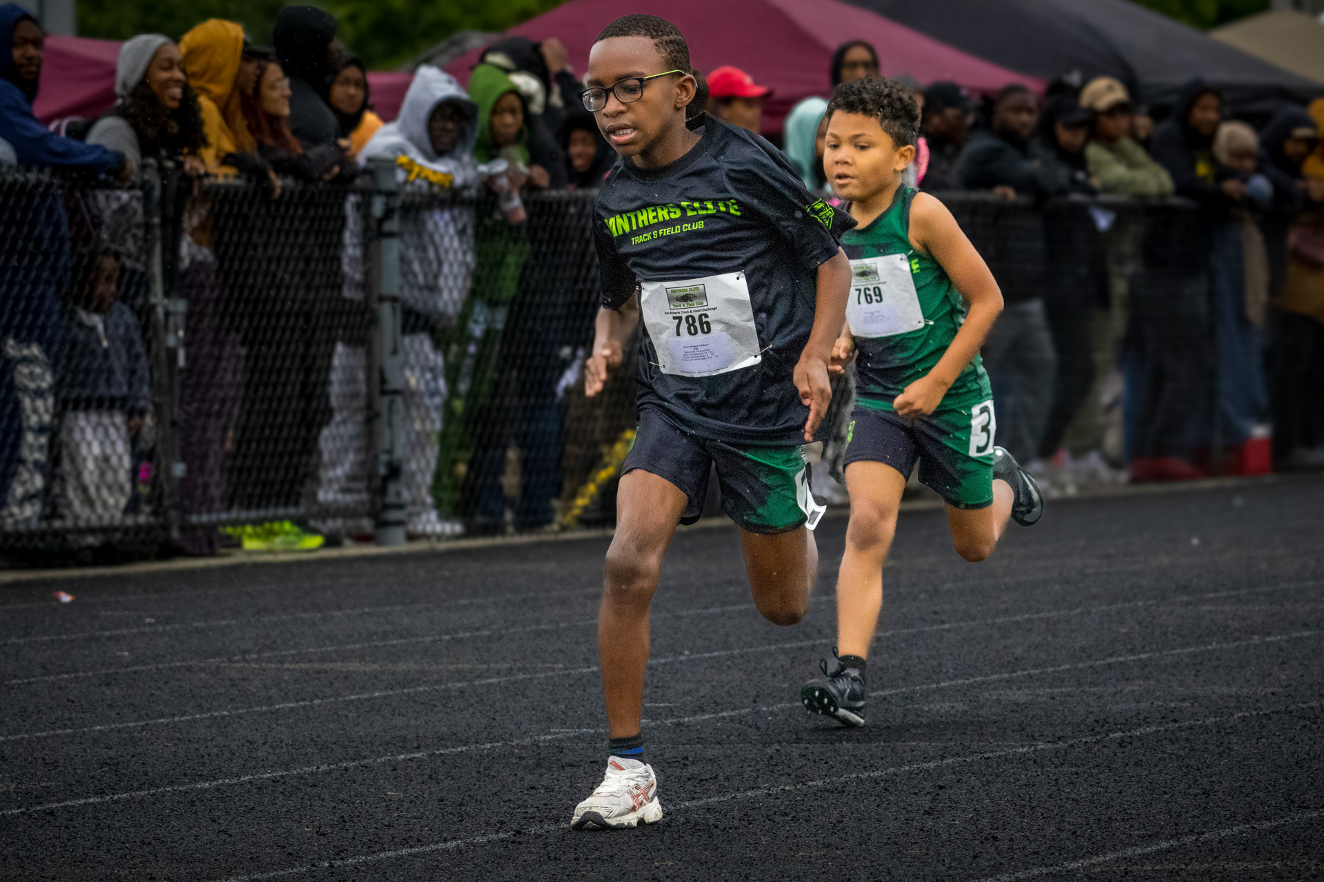 Young male athletes competing in a sprint race at a track meet.