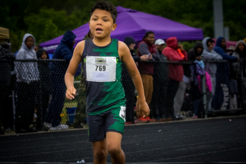 Young boy running in a track race, wearing a green and black uniform with bib number 769.