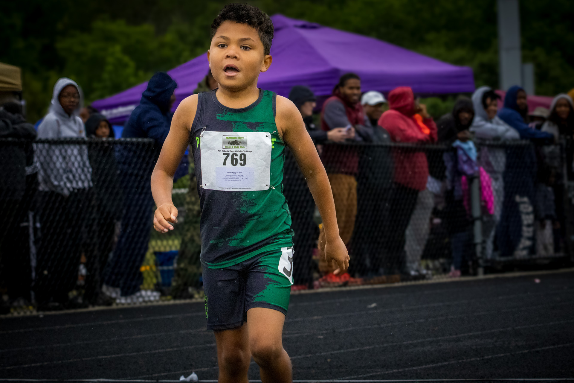 Young boy running in a track race, wearing a green and black uniform with bib number 769.