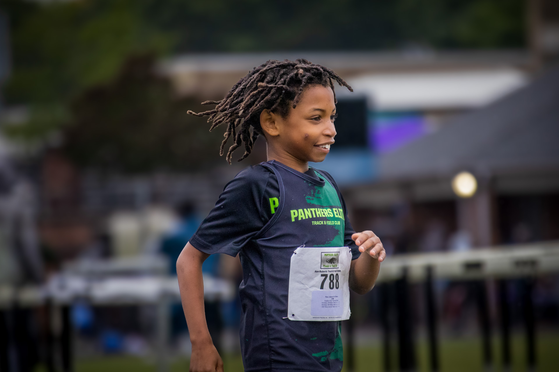 Young female athlete running at a track event, wearing Panthers Elite gear.