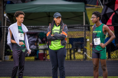 Coach with two young athletes at Panthers Elite Track & Field event, preparing for race.