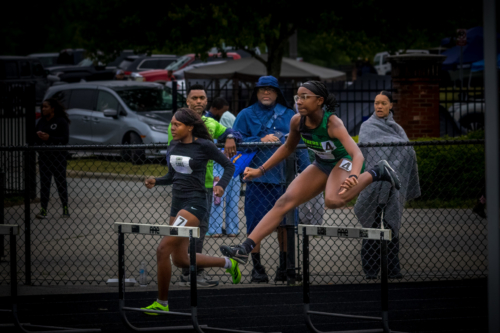 Female athlete jumping over hurdles during a track meet.