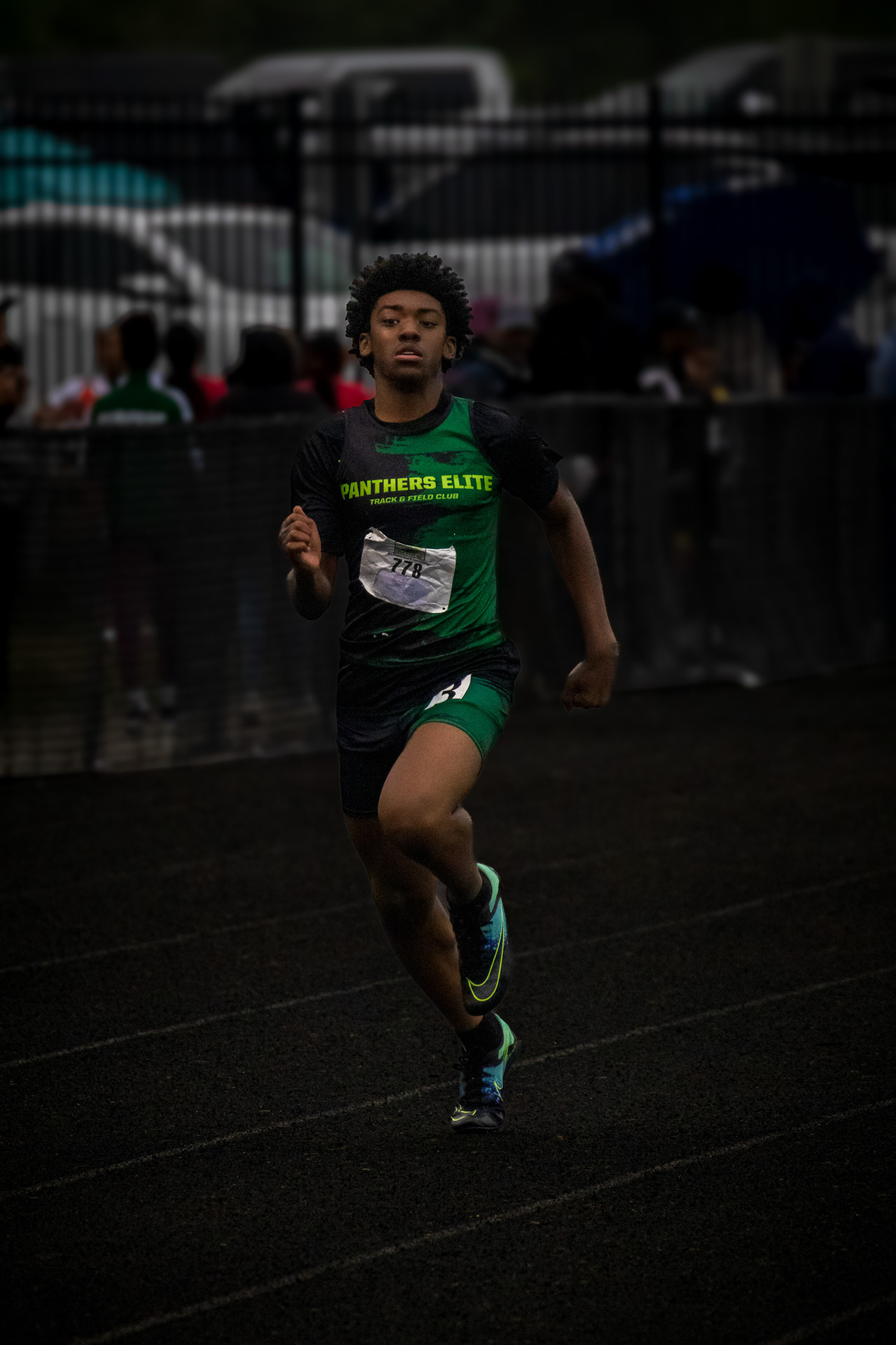 Young male athlete running on track during a meet, wearing Panthers Elite gear.