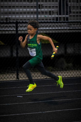 Young athlete running on track with baton during a race.
